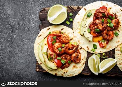 Fajitas in tortillas with fried shrimps, bell peppers and onion served up with avocado and green onions on wooden cutting board, top view, food background with space for a text