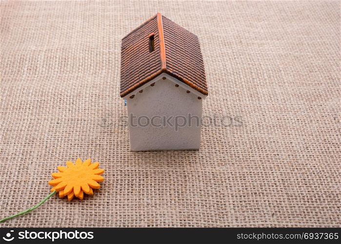 Fake flower by a model house on a brown color background