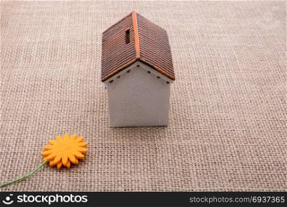 Fake flower by a model house on a brown color background