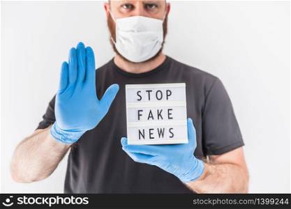 Fake news infodemics during Covid-19 pandemic concept. Man wearing protective mask and medical gloves on hands holding lightbox with text Stop fake news. People want to know truth about coronavirus