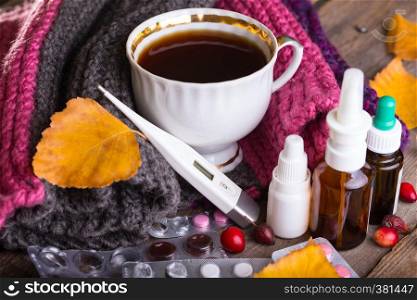 Fall and health care. cup of tea, pills and thermometer on a wooden background