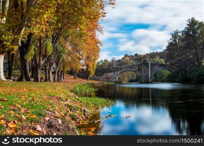 Fall foliage and medieval Roman bridge reflected on the water in the Galician village of Allariz, Ourense.