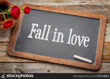 Fall in love advice - white chalk text on a vintage slate blackboard with red roses against rustic wood
