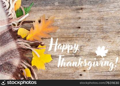 Fall leaves with woolen plaid on old wood, autumn background with happy thanksgiving greetings. Fall leaves autumn background