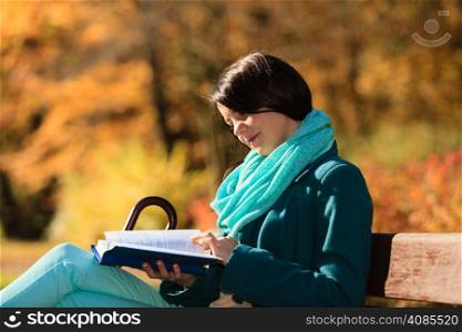Fall lifestyle concept. Casual young woman girl relaxing in autumnal park reading book. Golden colorful leaves background