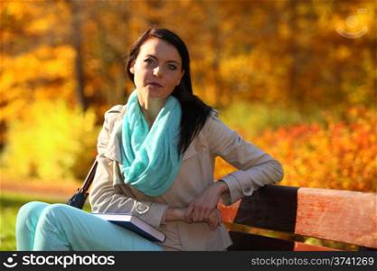Fall lifestyle concept, harmony freedom. Casual young woman girl relaxing in autumnal park sitting on bench with book. Golden colorful leaves background