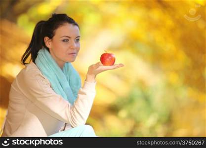 Fall lifestyle concept, harmony freedom. Casual young woman girl relaxing in autumnal park eating red apple. Golden colorful leaves background