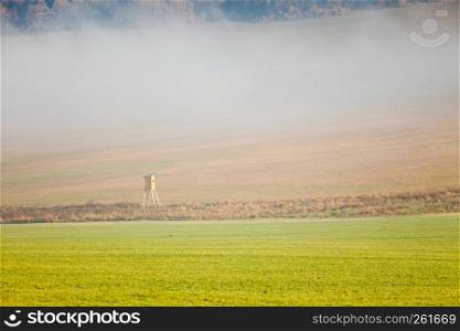 Fall misty landscape. Country field scenery with wooden hunter ambush on autumn day at morning time. Country field fog landscape on autumn day