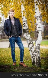 Fall season and people concept. Full length of young stylish fashionable man posing against autumn birch trees. Yellow leaves background