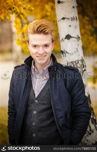 Fall season and people concept. Portrait of young smiling stylish fashionable man in plaid shirt and jacket against autumn birch trees. Yellow leaves background