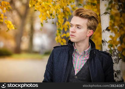 Fall season and people concept. Portrait of young stylish fashionable man in plaid shirt and jacket against autumn birch trees. Yellow leaves background