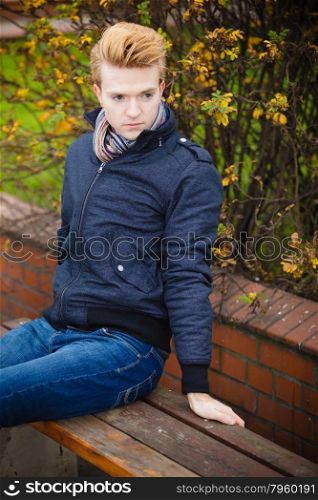 Fall season and people concept. young stylish fashionable man relaxing on bench in autumn park. Yellow leaves background