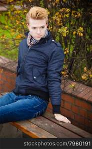 Fall season and people concept. young stylish fashionable man relaxing on bench in autumn park. Yellow leaves background