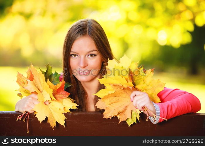 Fall season. Portrait of happy girl young woman holding colorful leaves sitting on bench in autumnal park forest. Outdoor.