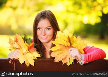 Fall season. Portrait of happy girl young woman holding colorful leaves sitting on bench in autumnal park forest. Outdoor.
