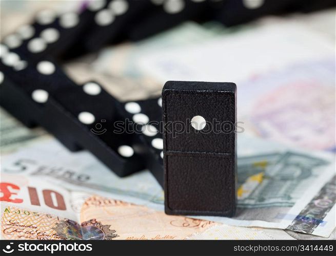 Fallen dominoes on pound, euro and dollar bank notes illustrating banking crisis