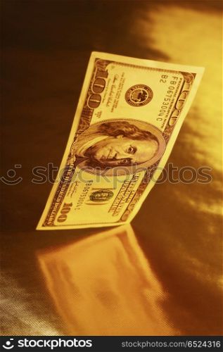Falling 100 dollar denominations in reflection on a gold background. Currency imaginations