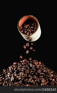 Falling coffee beans from a white cup and freshly roasted coffee beans on the table, vertical frame on a black background