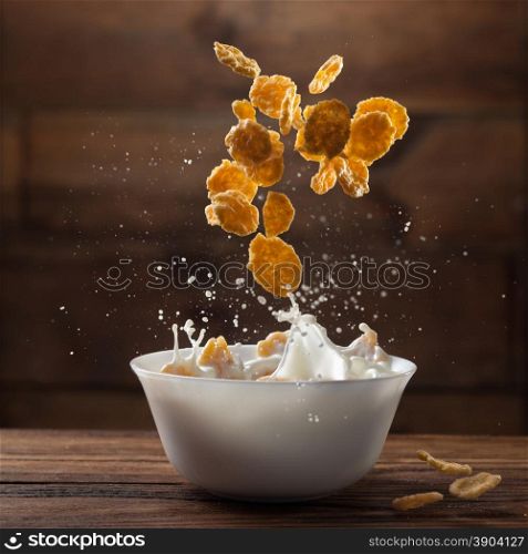 Falling corn flakes with milk splash on wooden background. Falling corn flakes with milk splash on wood