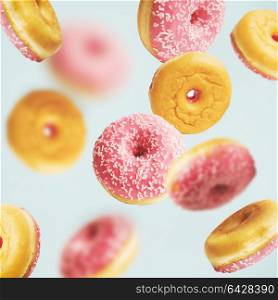 Falling or flying pink glazed doughnuts with sprinkles at pastel blue background , creative layout or pattern