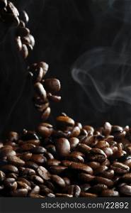 Falling roasted coffee beans with steam on black