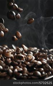 Falling roasted coffee beans with steam on black