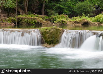 Falls on the mountain behind a forest with trees and rocks.