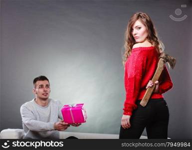 False feelings, relations problem. Trusting guy giving present pink box to misleading girl. Insincere woman holding axe behind her back