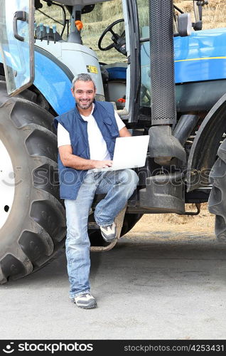 Famer with laptop computer stood by tractor