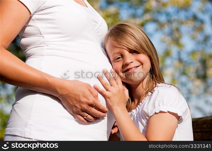 Family affairs - Girl is touching round belly of her pregnant mother in eager anticipation of the new child