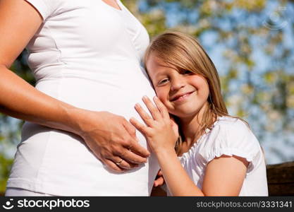 Family affairs - Girl is touching round belly of her pregnant mother in eager anticipation of the new child