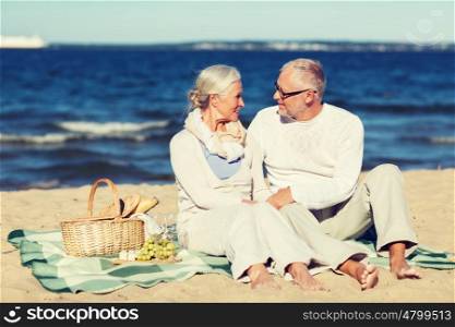 family, age, holidays, leisure and people concept - happy senior couple with picnic basket sitting on blanket on summer beach
