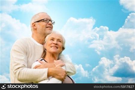 family, age, love, relations and people concept - happy senior couple hugging over blue sky and clouds background