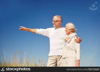 family, age, romance, leisure and people concept - happy senior couple pointing finger to something outdoors