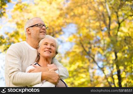 family, age, season and people concept - happy senior couple hugging over autumn trees background