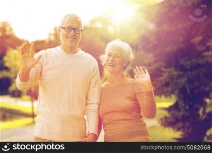 family, age, tourism, gesture and people concept - senior couple waving hands in city park. senior couple hugging in city park