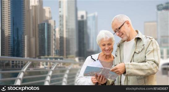 family, age, tourism, travel and people concept - happy senior couple with map and city guide on street over dubai city waterfront background