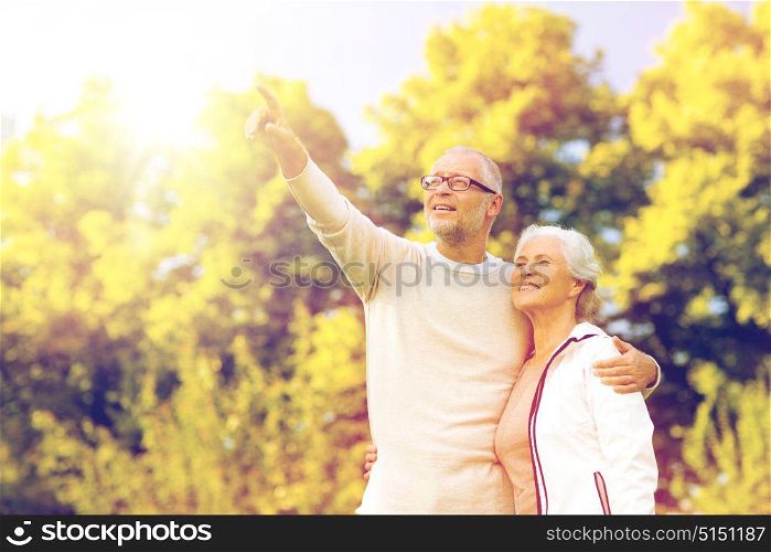 family, age, tourism, travel and people concept - senior couple hugging and pointing finger in park. senior couple hugging in park
