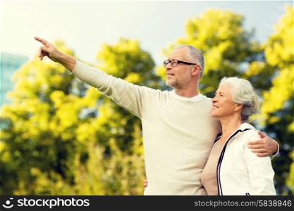 family, age, tourism, travel and people concept - senior couple hugging and pointing finger in park