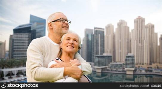 family, age, tourism, travel and people concept - senior couple hugging over dubai city waterfront background