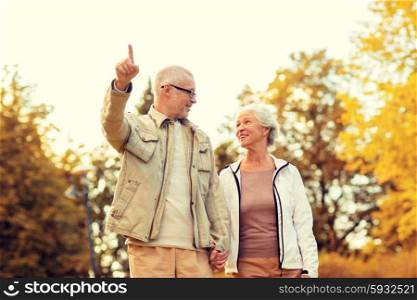 family, age, tourism, travel and people concept - senior couple pointing finger and walking in park