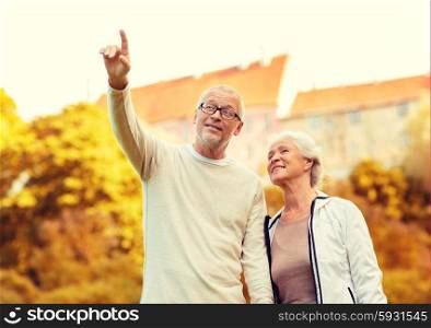 family, age, tourism, travel and people concept - senior couple pointing finger in city park
