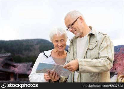 family, age, tourism, travel and people concept - senior couple with map and over asian village and mountains landscape background