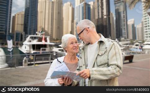 family, age, tourism, travel and people concept - senior couple with map and city guide over dubai harbor or waterfront background