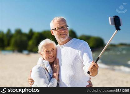 family, age, travel, technology and people concept - happy senior couple with smartphone selfie stick photographing and hugging on summer beach