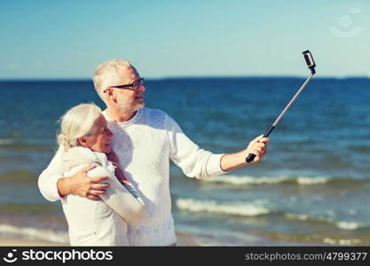 family, age, travel, technology and people concept - happy senior couple with smartphone selfie stick photographing and hugging on summer beach