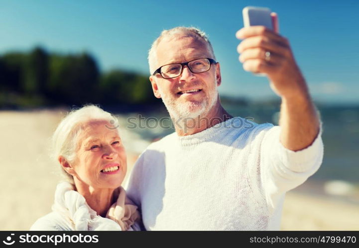 family, age, travel, technology and people concept - happy senior couple with smartphone taking selfie and hugging on summer beach