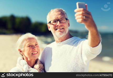 family, age, travel, technology and people concept - happy senior couple with smartphone taking selfie and hugging on summer beach