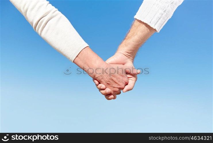 family, age, travel, tourism and people concept - close up of senior couple holding hands over blue sky background