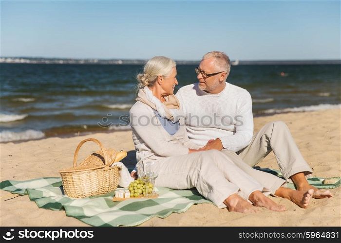 family, age, travel, tourism and people concept - happy senior couple having picnic and talking on summer beach